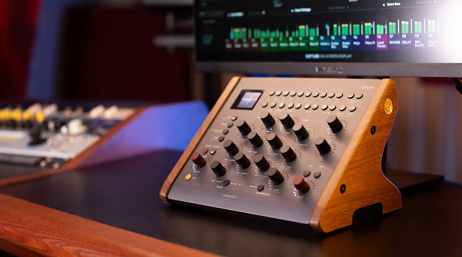 Softube Console 1 Compact controller with wooden side panels angled on desk, showing faders and knobs with DAW display behind