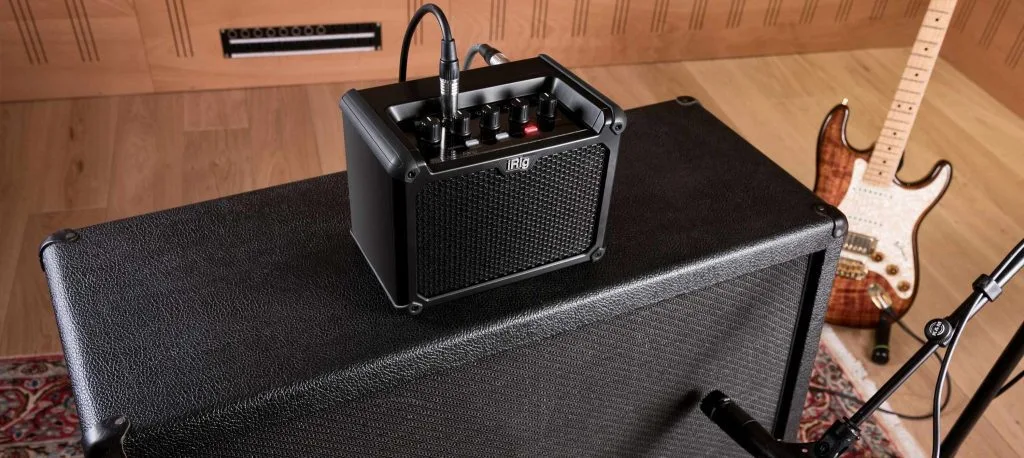 iRig Micro Amp black portable guitar amplifier on amplifier cabinet with bass guitar nearby, overhead view