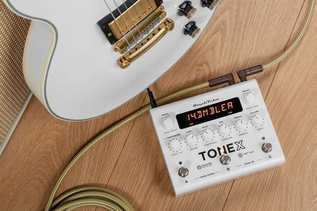 TONEX Anniversary LE white pedal with digital display connected to electric guitar with cream-colored cable on wooden surface