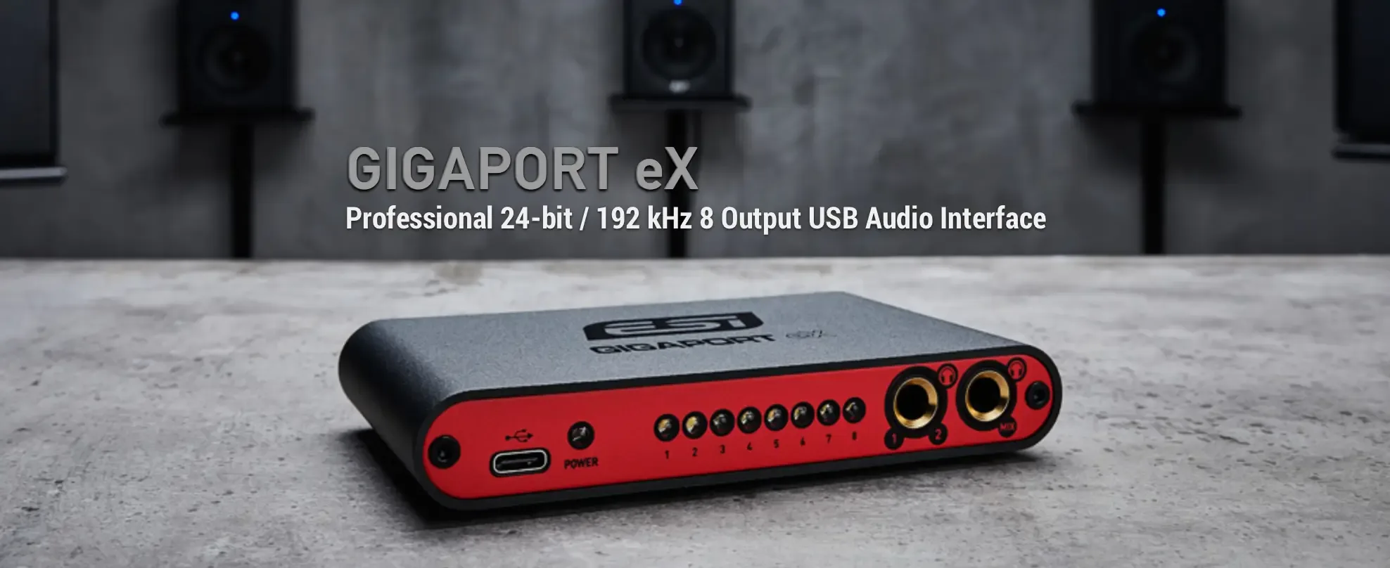 ESI GigaPort eX audio interface angled right, showing red front panel with 8 output buttons and gold connectors on concrete surface