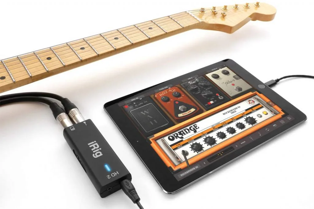 iRig HD2 audio interface connected via cable to tablet displaying guitar amp simulation app, with electric guitar neck visible above
