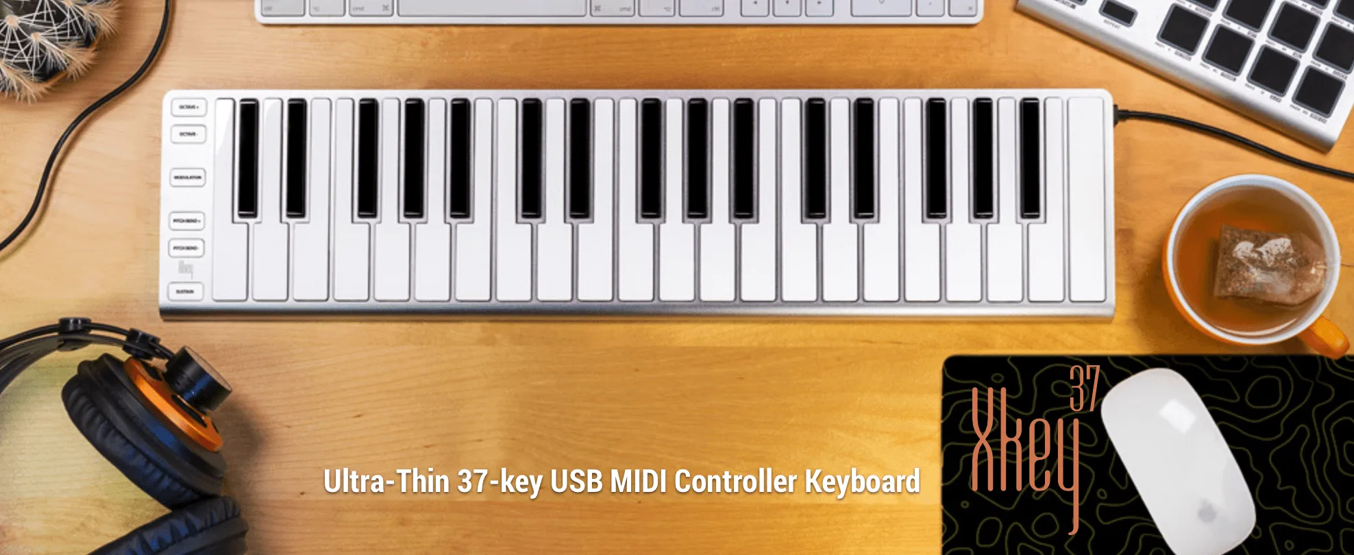 White 37-key USB MIDI keyboard on wooden desk with headphones, coffee cup, and mouse in workspace setup