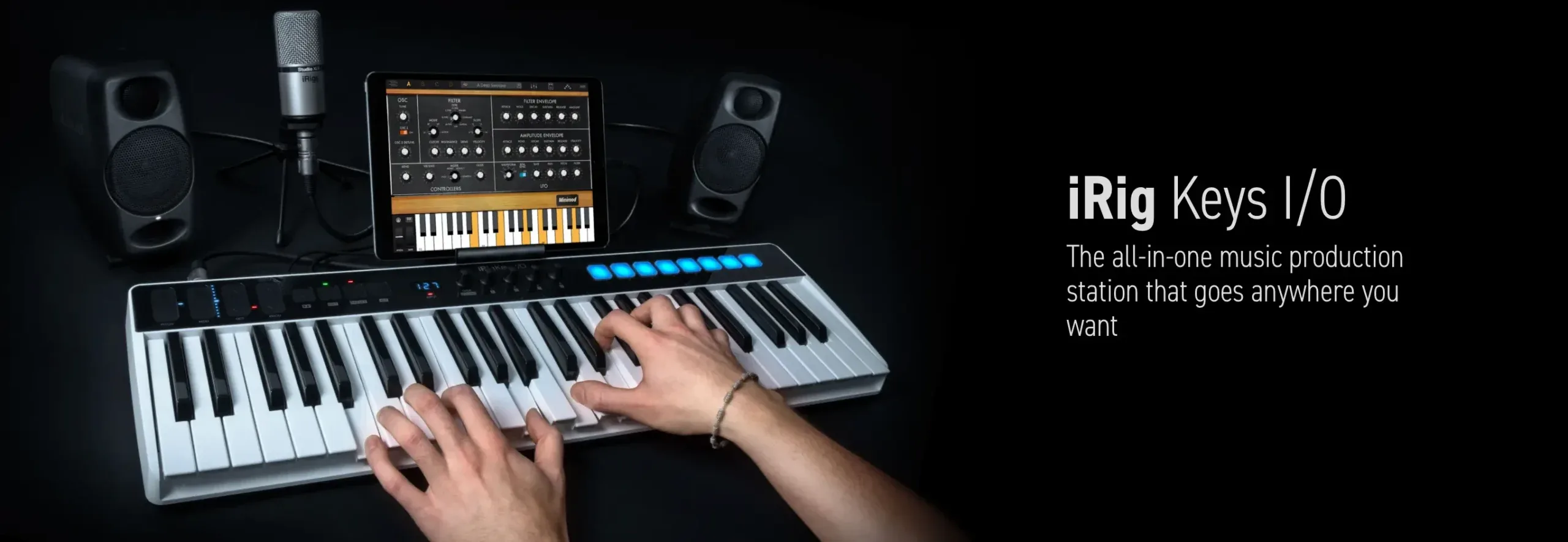 Hands playing an iRig Keys I/O keyboard controller in a studio with monitors, a microphone and a synth plug-in on a tablet