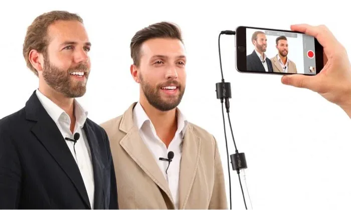 Two men in business attire shown being recorded on smartphone with iRig Mic Lav 2 lavalier microphones visible as thin black cables