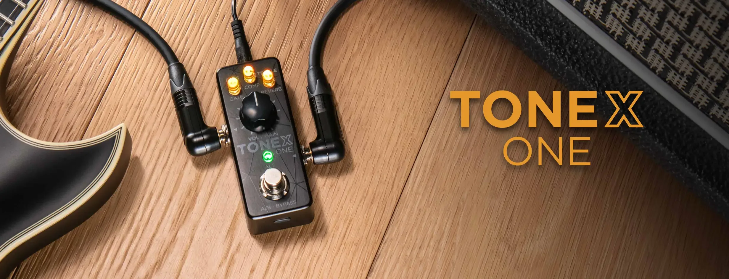 TONEX ONE compact guitar pedal on wooden surface with connected earbuds and partial acoustic guitar visible