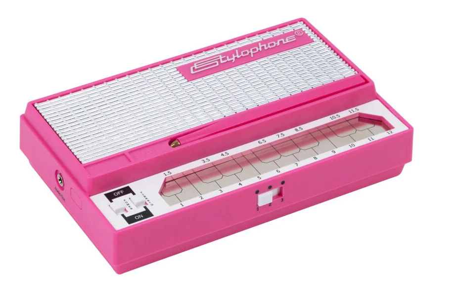 Bright pink Stylophone synthesizer shown at an angle, displaying the stylus pen and numbered keyboard scale on white background.