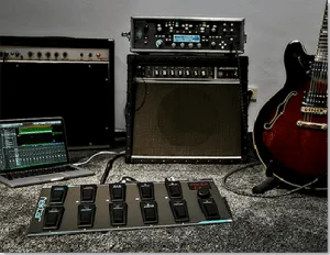 Nektar Pacer MIDI controller with eight faders on grey surface, flanked by amplifiers and semi-hollow body guitar