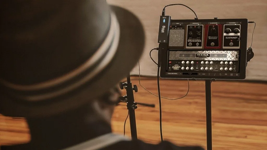 iRig HD2 guitar interface mounted on stand next to amplifier modeling pedalboard, wooden floor setup