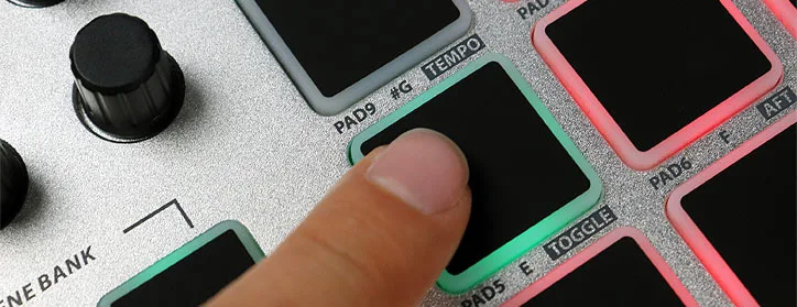 Top-down view of ESI Xjam pad controller with finger pressing green-bordered pad, pink and black pads visible, knob above