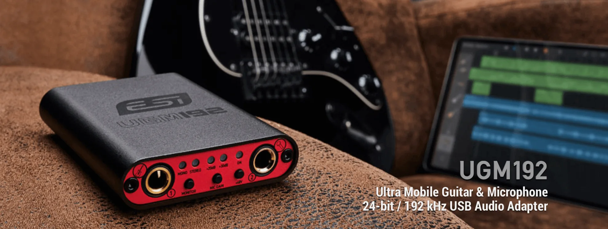 ESI UGM192 USB audio adapter with red faceplate and dual gold knobs, positioned on brown fabric with black guitar and DAW display visible behind