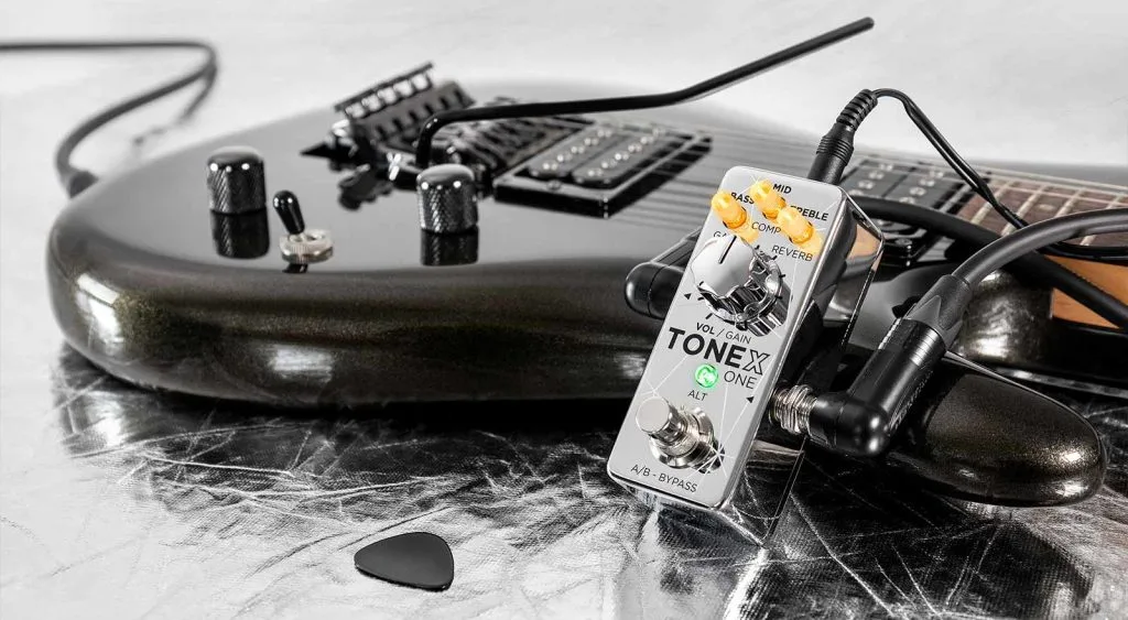 White TONEX ONE pedal with control knobs positioned on marble surface among guitar cables and black amplifier equipment