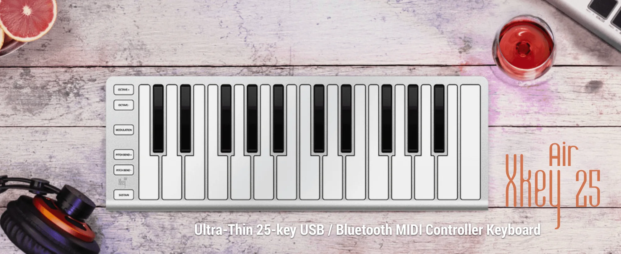 ESI Xkey Air 25 ultra-thin 25-key MIDI keyboard on white wood desktop with grapefruit slice, headphones, and drink visible